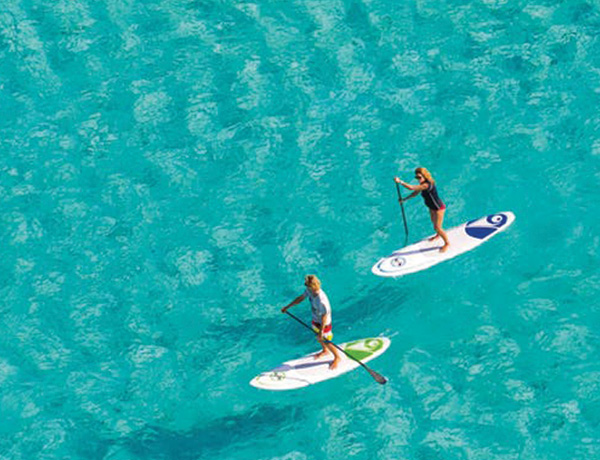 Aerial shot of a couple paddle boarding in clear blue water.